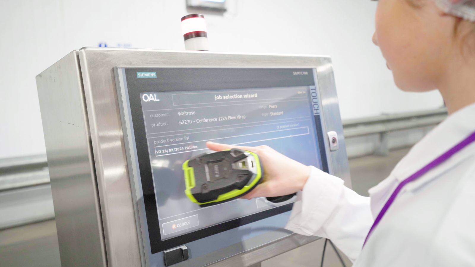 Operator using an OAL Connected job selection screen on a stainless steel line panel while holding a handheld scanner